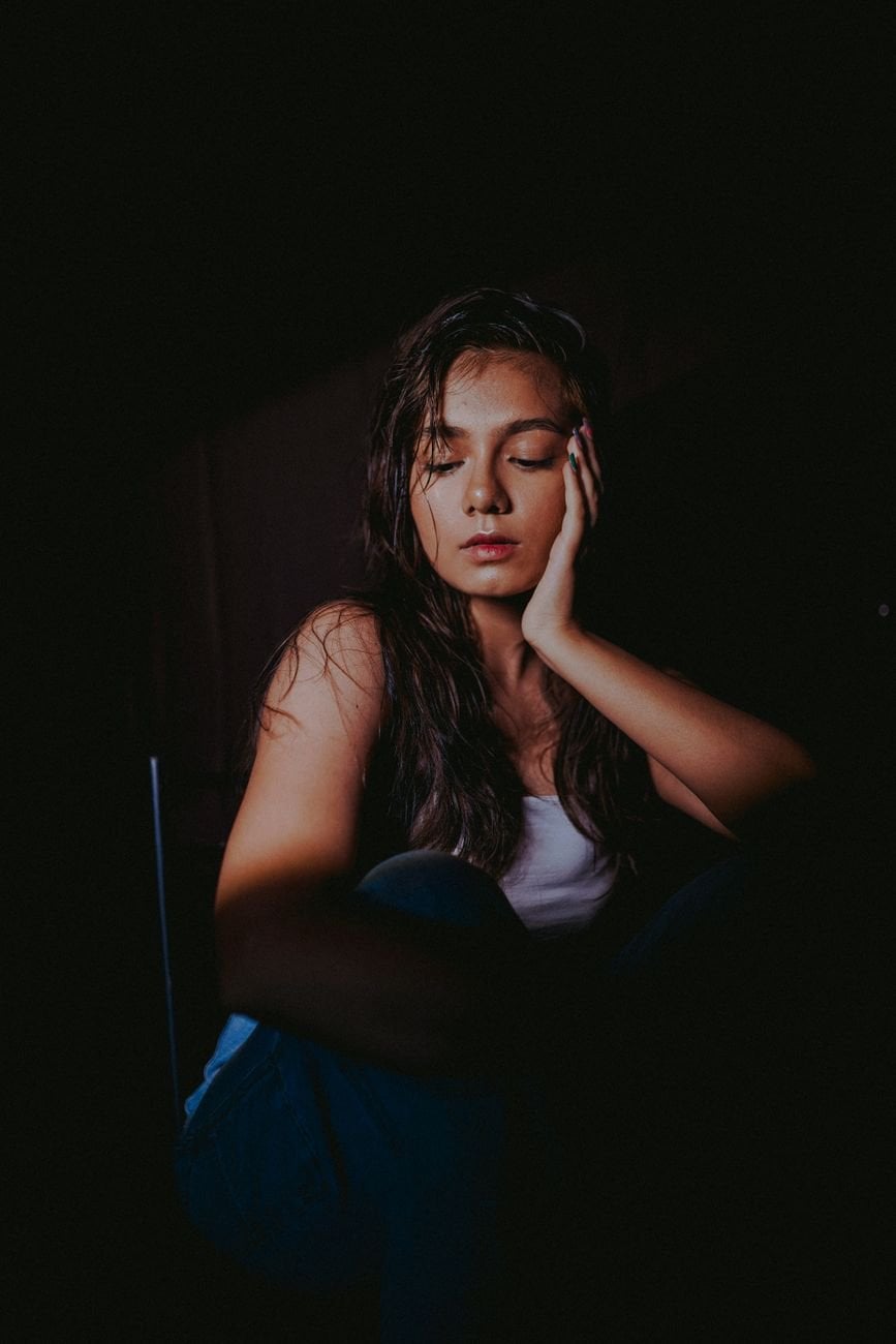 Moody portrait of a woman sitting with eyes closed, captured in a studio spotlight.